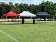 Three Rocket Canopy pop-up tents in red, white, and black set up on a sports field, showcasing their sturdy frames and weather-resistant design.